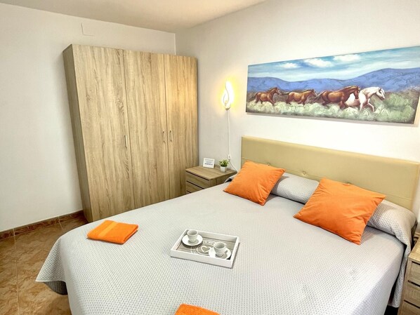 A neatly made bed with a tray of breakfast items, a wooden wardrobe, and a painting of horses on the wall. - APARTBEACH NEW BONA NOVA BEACH (Salou)