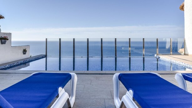An infinity pool with clear blue water, two blue lounge chairs, and a view of the ocean. - Villa with pool located in the south of Spain (Salobreña)