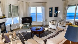 A modern living room with a large sofa, a coffee table, and a TV. There are large windows with ocean views. - Villa with pool located in the south of Spain (Salobreña)