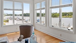 A room with large windows overlooking a marina, a wooden floor, and a brown chair. - Waterfront Views & Boat Slip, Blackwell Point #C (Oriental)