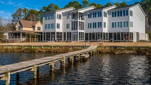 A waterfront property with a dock extending into the water, a large building with multiple windows and balconies, and a smaller house adjacent to it. - Waterfront Views & Boat Slip, Blackwell Point #C (Oriental)