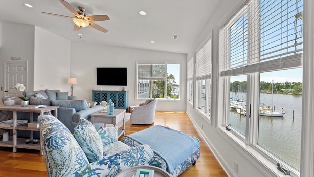 A spacious living room with a large window overlooking a body of water, a ceiling fan, and a flat-screen TV mounted on the wall. - Waterfront Views & Boat Slip, Blackwell Point #C (Oriental)