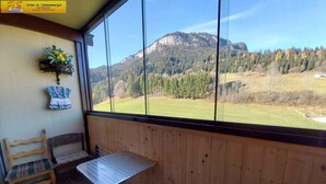A wooden-paneled room with a table and chairs, a window with a mountain view, and a wall-mounted flower arrangement.