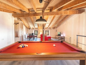 A pool table with balls, a red sofa, a television, and wooden beams in a room.