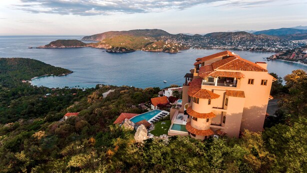 Una villa costera con piscina, rodeada de exuberante vegetación y vistas al mar.