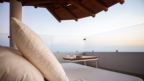 Un balcón con sofá y almohadones, una mesa con vasos y un plato, y vista al horizonte.