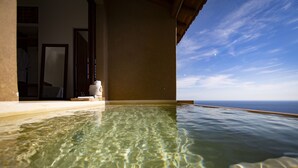 Una piscina infinita cristalina con vistas al océano, una terraza de madera y una estatua blanca.
