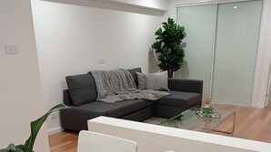 A modern living room with a grey sectional sofa, a glass coffee table, and a potted plant. - 'LITTLE LAKE LODGE' - on Warilla Beach / Little Lake (Warilla)