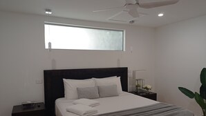 A modern bedroom with a large bed, a ceiling fan, a bedside table with a lamp, and a window. - 'LITTLE LAKE LODGE' - on Warilla Beach / Little Lake (Warilla)