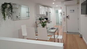 A modern, well-lit dining area with white furniture, a glass table, and a hanging plant. - 'LITTLE LAKE LODGE' - on Warilla Beach / Little Lake (Warilla)