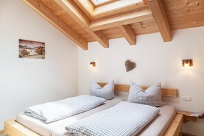 Une chambre avec deux lits, des poutres en bois, un puits de lumière, une applique murale et un tableau encadré.