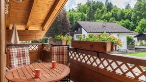 Eine Holzterrasse mit rundem Tisch und Stühlen, ein Holzzaun und Blick auf Häuser und Bäume.