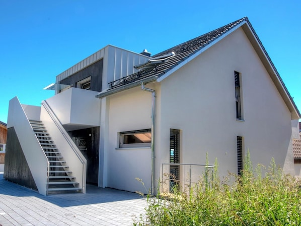 Una casa moderna de dos pisos con una escalera que conduce al nivel superior, un balcón y cielo despejado.