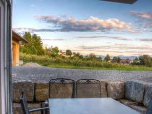 Un patio con mesa y sillas, con vistas a un paisaje rural con casas y montañas.