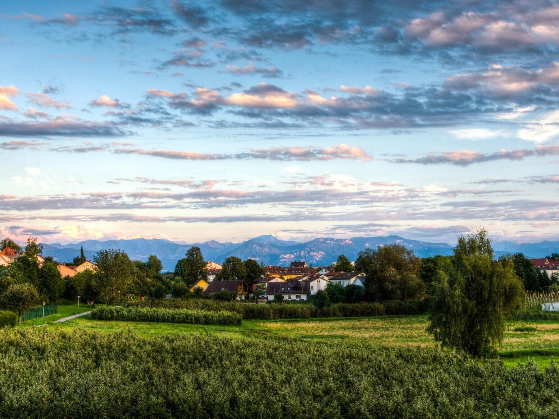 A rural landscape with houses, fields, and mountains in the background.