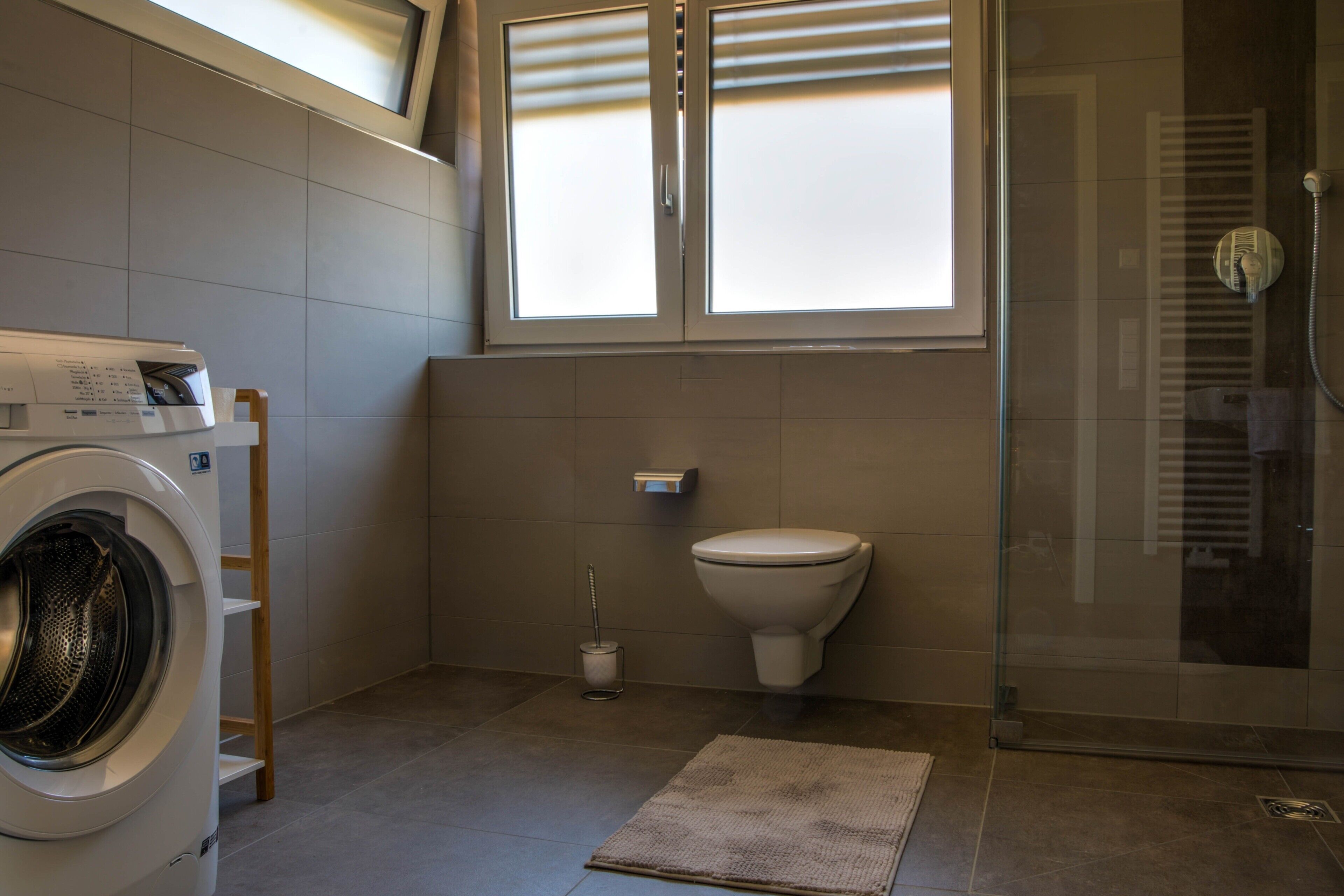 A bathroom with a washing machine, toilet, and glass shower enclosure.