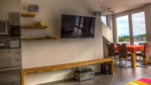 Un salon moderne doté d’un téléviseur à écran plat, d’étagères en bois, d’un banc et d’un coin repas avec des chaises et une table.
