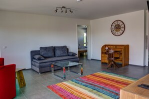 A modern living room with a grey sofa, a glass coffee table, a colorful striped rug, a wooden desk, and a wall clock. - "Alpenblick 2 - Holiday Apartment" with Mountain View (Bodolz)