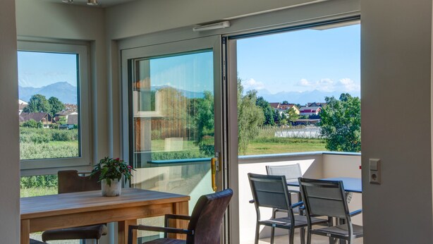 Un balcon avec une table et des chaises, une plante en pot et une vue sur les montagnes et la verdure.