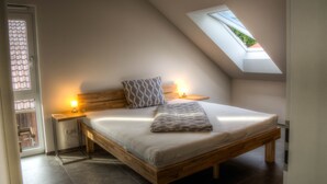 A bedroom with a sloped ceiling, a skylight, a bed with a headboard, two bedside tables with lamps, and a window.