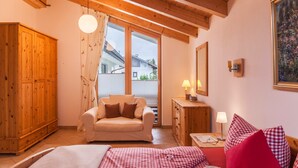 A cozy room with a wooden ceiling, a bed with checkered bedding, a sofa, a wooden wardrobe, and a window with curtains. - Vacation Home "Das Bergzeit" with Mountain View, Wi-Fi, Garden & Terrace (Farchant)