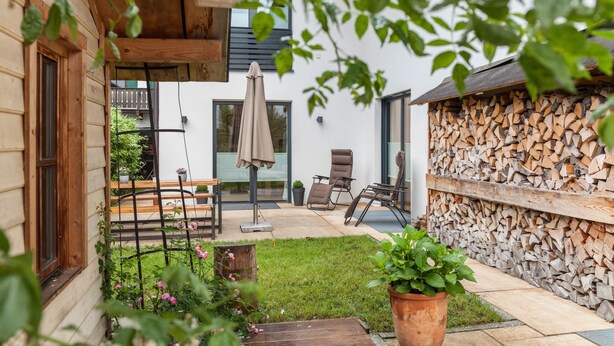 A wooden house with a patio, outdoor seating, and a firewood stack. - Vacation Home "Das Bergzeit" with Mountain View, Wi-Fi, Garden & Terrace (Farchant)