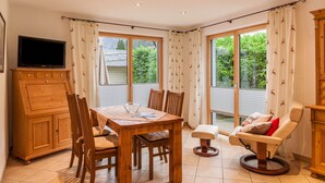 A dining area with a wooden table, chairs, a television, and a window with curtains. - Vacation Home "Das Bergzeit" with Mountain View, Wi-Fi, Garden & Terrace (Farchant)