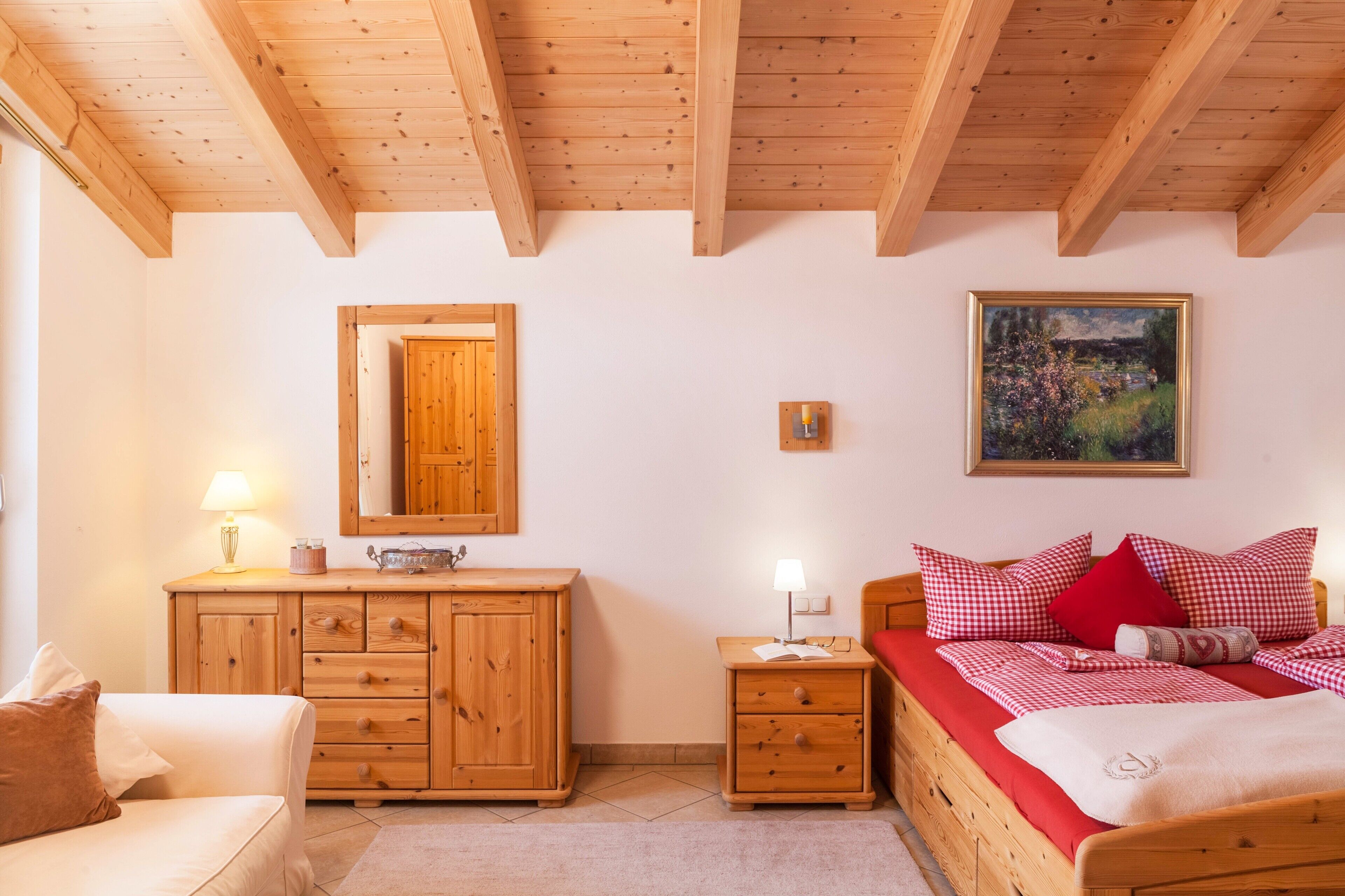 Ein Schlafzimmer mit Holzwäsche, einem Bett mit roter Bettwäsche, einem Nachttisch mit Lampe, einer Holzkommode und einem Bild an der Wand.