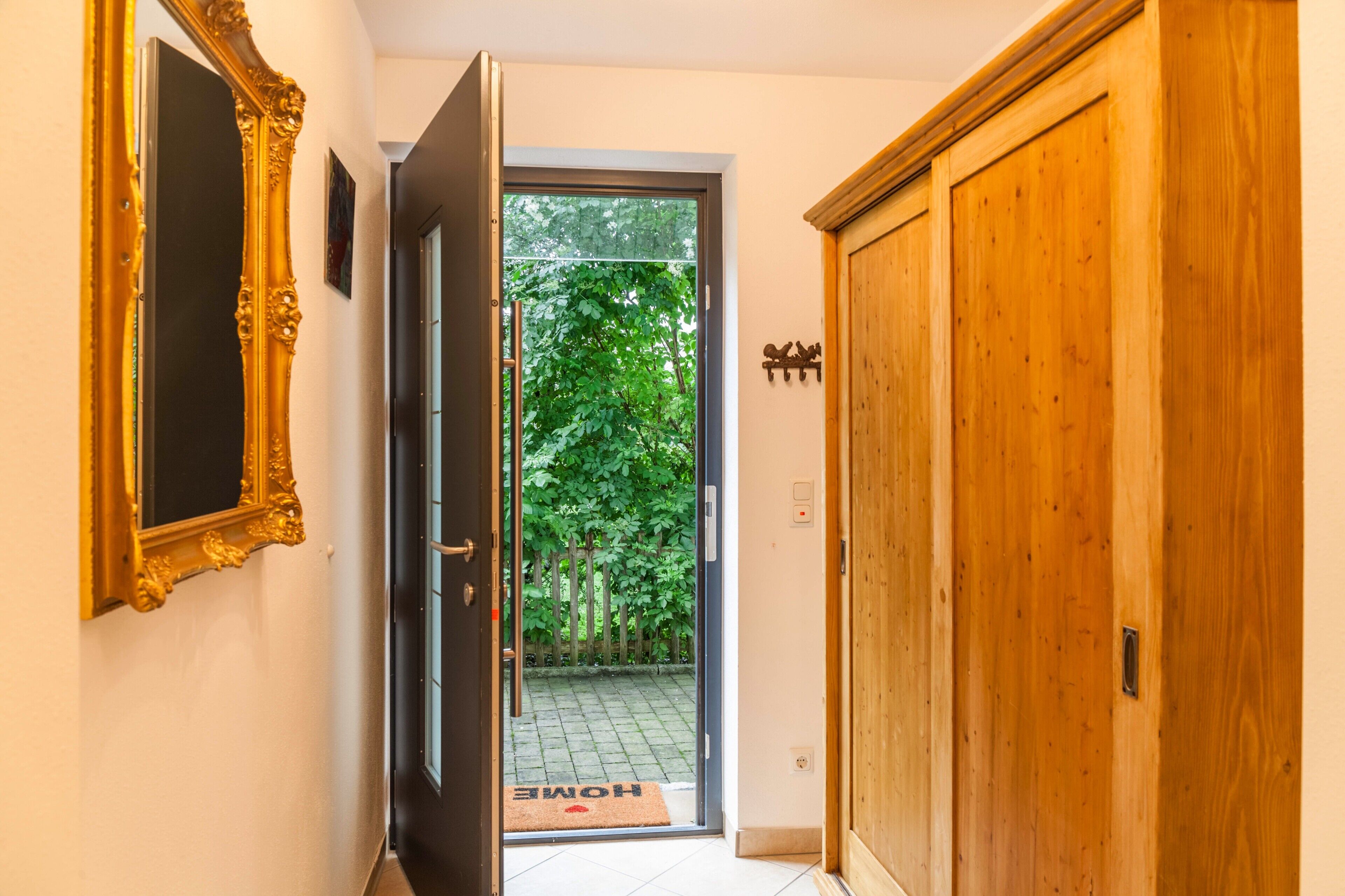 A hallway with a door leading to a garden, a doorbell, and a wooden door.