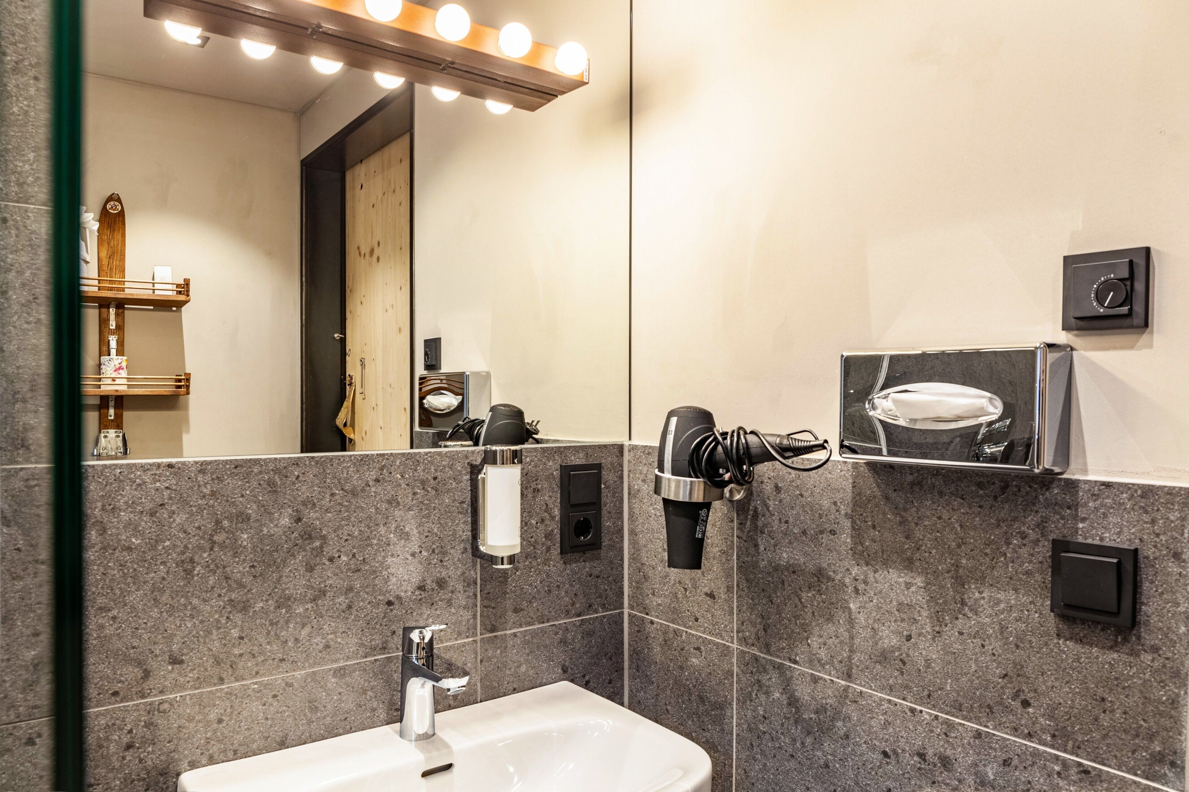 A bathroom with a mirror, vanity, sink, towel dispenser, and hairdryer.