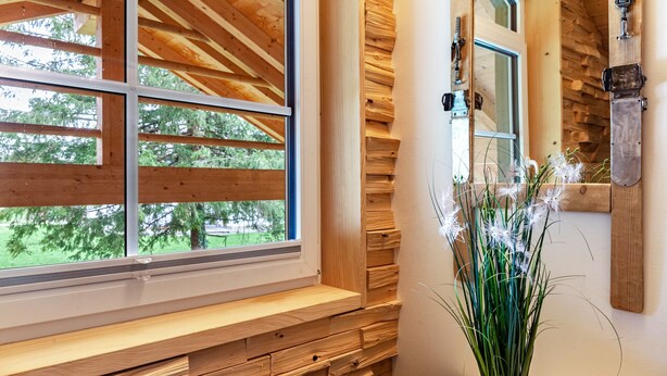 Un interior de madera con una ventana, un banco y una planta en maceta.