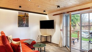 A living room with a red sofa, a small table, a flat-screen TV, and a sliding glass door leading to an outdoor deck. - Chalet Rauschn with mountain view with shared sauna, terrace, balcony; pet friendly (Farchant)