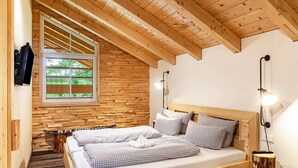 A bedroom with a sloped ceiling, wooden walls, a large window, two beds, bedside lamps, and a small table. - Chalet Rauschn with mountain view with shared sauna, terrace, balcony; pet friendly (Farchant)