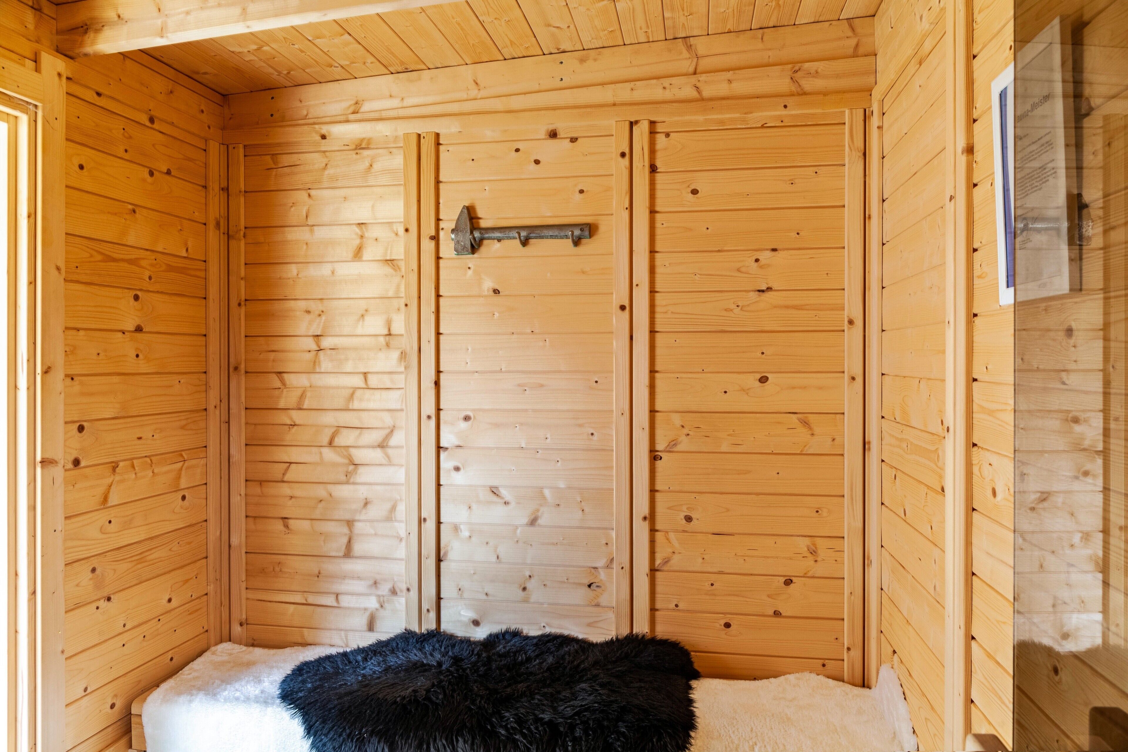 A wooden cabin interior with a bed, a door, and a window.
