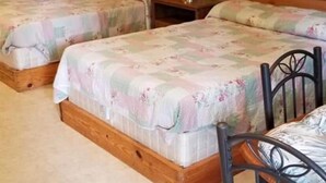 A room with two wooden beds, a small table, and a lamp.