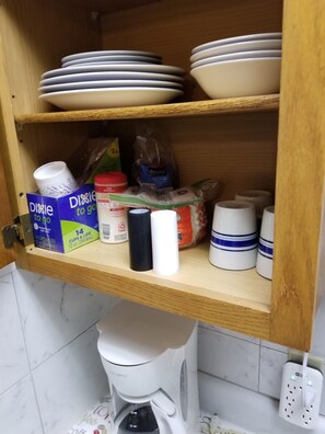 A kitchen cabinet with stacked plates, a coffee maker, and a box of disposable cups. - Cabin 2    2 double beds (Piedmont)