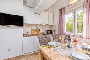 Une cuisine moderne avec des meubles blancs, une table à manger en bois préparée pour deux personnes et un téléviseur fixé au-dessus du comptoir.