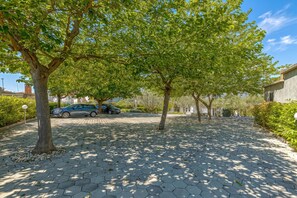 A paved walkway with trees, a parked car, and a building in the background. - Apartment Tonka 220m from the beach, Okrug Gornji, Croatia (Okrug Gornji)