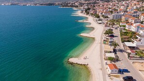 Ein Luftbild einer Küstenstadt mit einem langen, schmalen Strand, klarem, blauem Wasser und Wohngebäuden entlang der Küste.