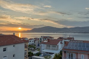 Ein Küstenwohngebiet mit Häusern, deren Dächer mit roten Ziegeln gedeckt und mit Solaranlagen ausgestattet sind, mit Blick auf ein Gewässer und ferne Berge.