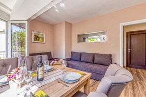 Un salon moderne comprenant un coin repas, un canapé, une table dressée pour deux personnes et un tableau accroché au mur.