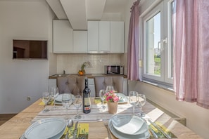 Un comedor con una mesa preparada para cuatro personas, una botella de vino y un jarrón de flores.