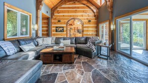 A log cabin interior with a stone floor, wooden walls, a large wooden ceiling, and a stone fireplace. - Large Grand Bend Getaway. Swim, Golf, Relax (South Huron (Munic))
