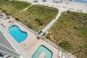 A pool area with a small pool and a larger pool, surrounded by a deck and a pathway leading to the beach.