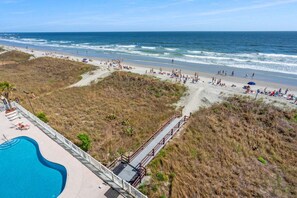 Een strand met een zwembad en een houten looppad.