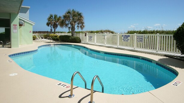 A swimming pool with a 5 ft depth marker, a lifeguard station, and a white fence with warning signs. - Welcome to PARADISE POINTE, your ultimate oceanfront retreat in North Myrtle Beach (North Myrtle Beach)