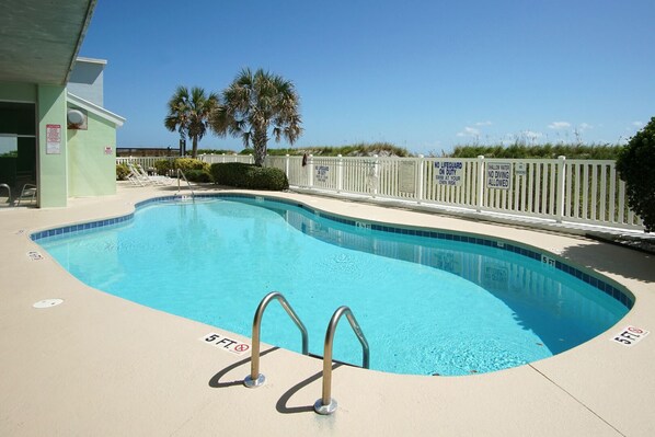 A swimming pool with a 5 ft depth marker, a lifeguard station, and a white fence with warning signs.