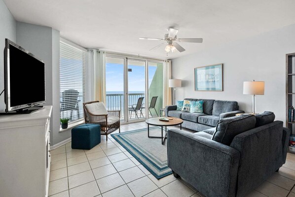 A modern living room with a flat-screen TV, a grey sofa, a coffee table, and a ceiling fan.