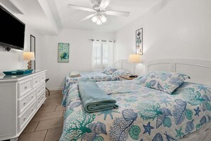 A bedroom with two beds, a ceiling fan, a TV, and a dresser.