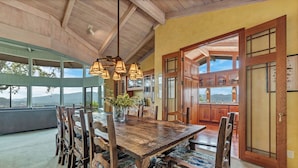A spacious dining area with a large wooden table and chairs, a hanging light fixture, and a view of the mountains through large windows. - Escape to “Casa Paradiso” in the Napa Valley! (Calistoga)